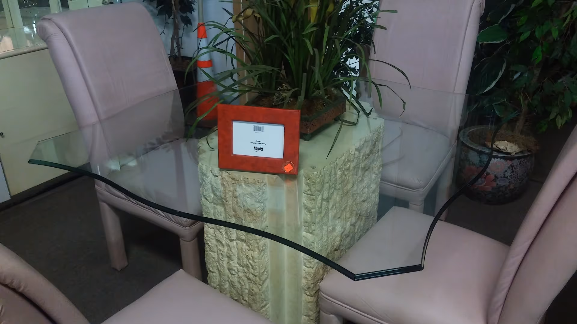 Indoor lounge area with curved glass table on a stone pedestal, pink cushioned chairs, and plants.