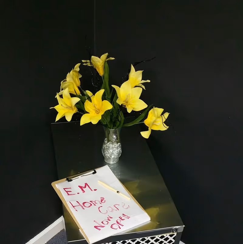Yellow lilies in a glass vase on a metallic counter against a dark wall.