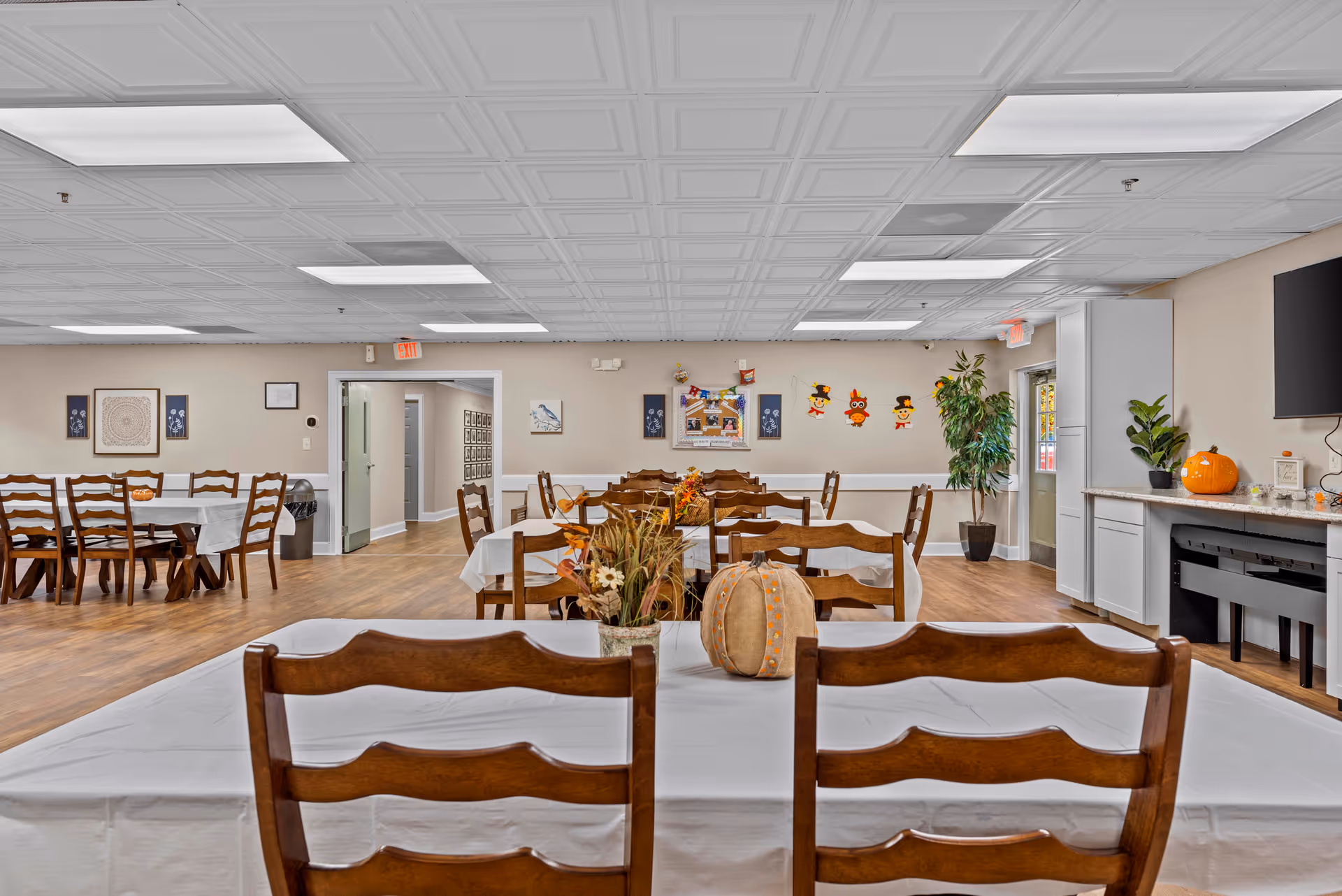 A spacious dining room with white-tablecloth tables and fall-themed centerpieces.