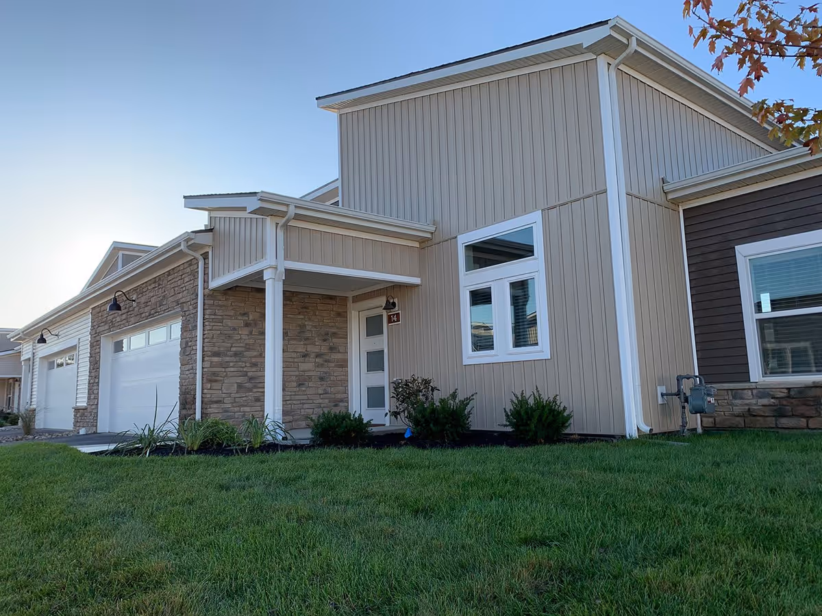 Front exterior of a modern townhouse-style building with garages, a covered entry porch, and a green lawn.
