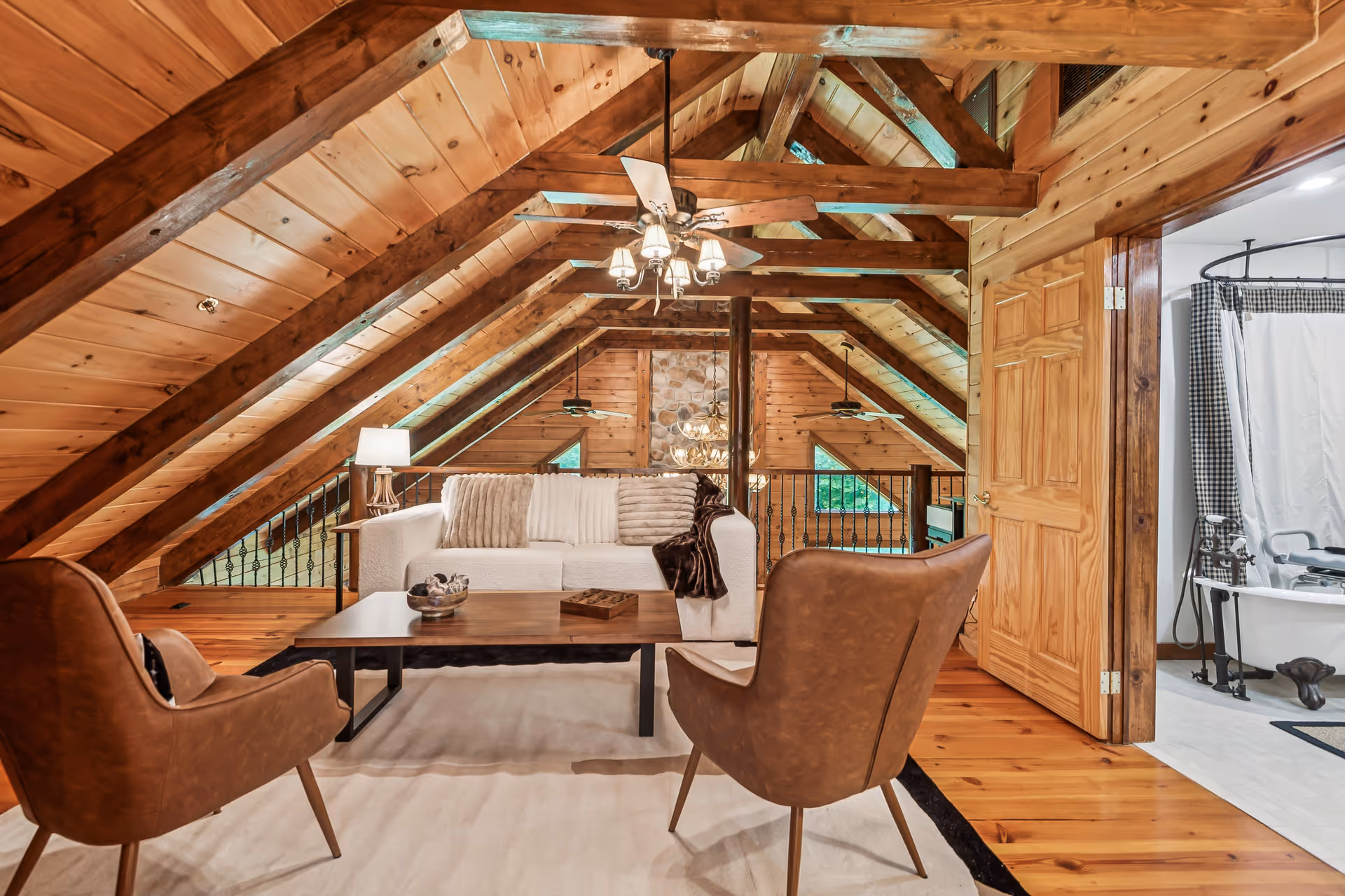Rustic attic living room with exposed wooden beams, seating, and a doorway to a bathroom.