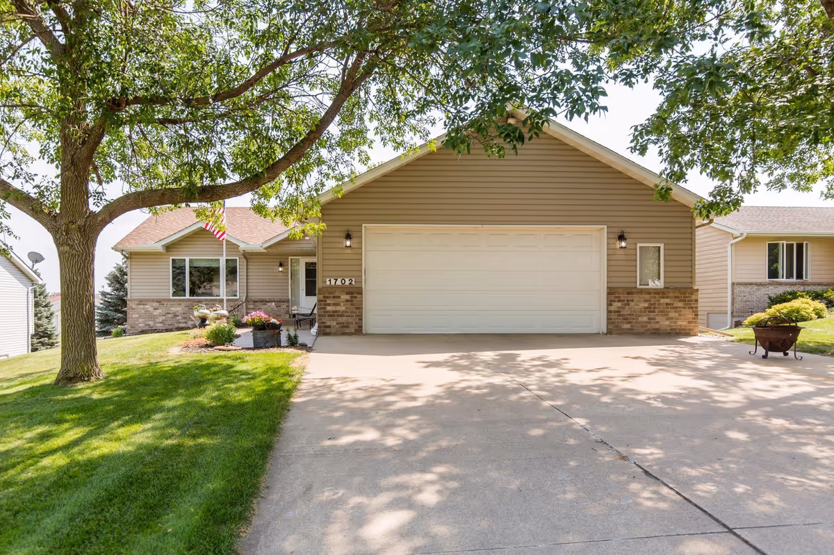 Front view of a suburban house with a two-car garage, driveway, and trees.