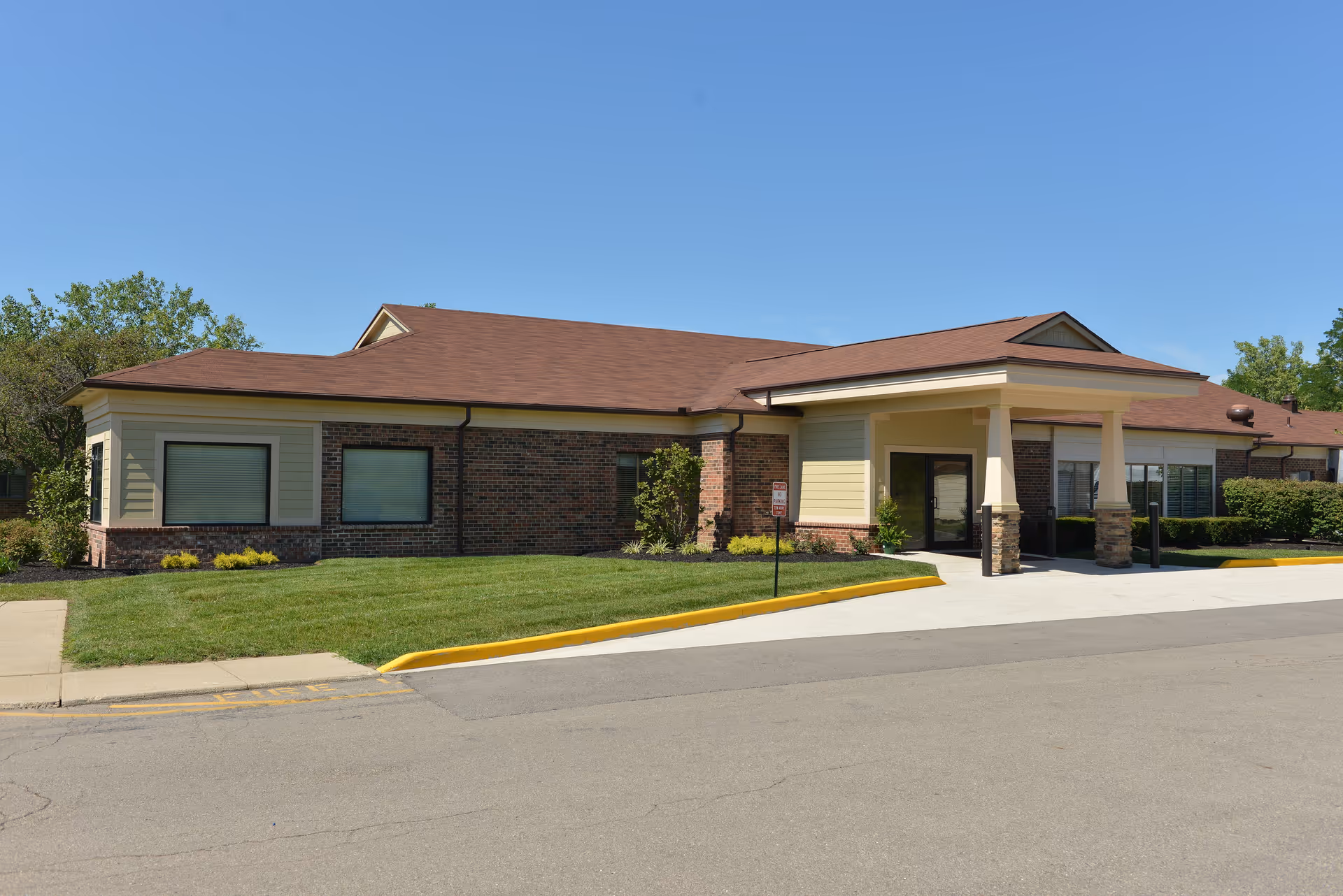Single-story senior living facility exterior with brick accents, manicured lawn, and covered entrance.