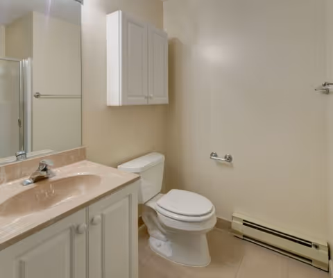 Bright bathroom with beige walls, sink, mirror, cabinet, shower, and toilet.
