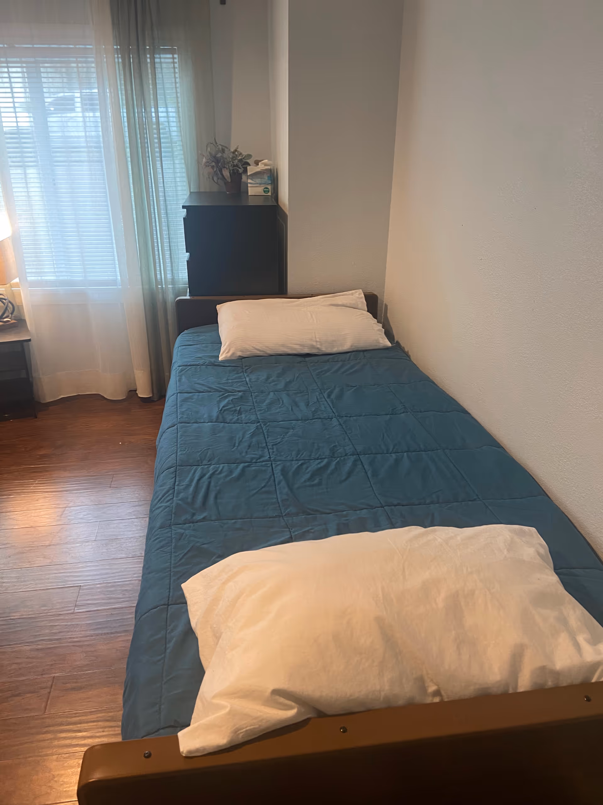 Cozy bedroom with blue quilted bed, white pillows, and a dresser near a window