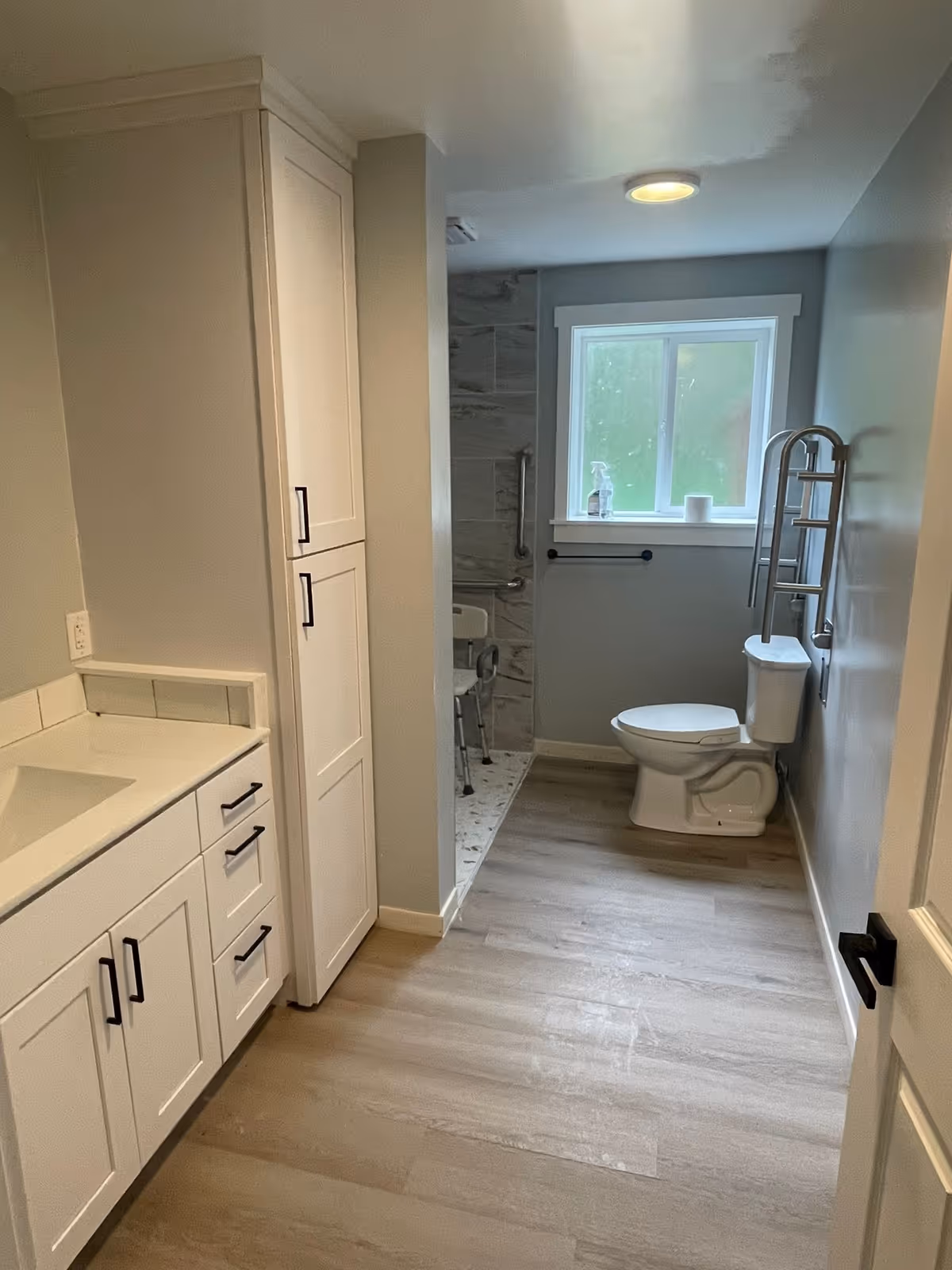 Bright accessible bathroom in a senior living facility with white cabinets, shower, and grab bars.