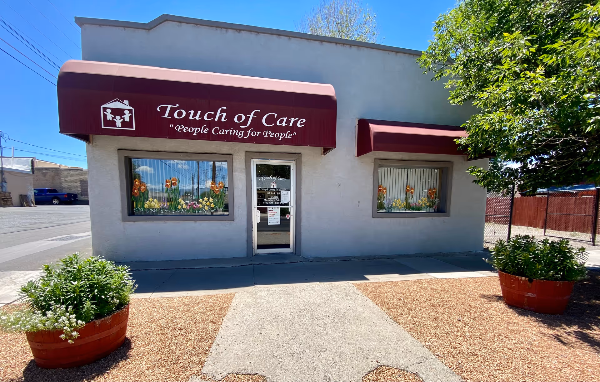 Facade of Touch of Care building with maroon awnings and planters.