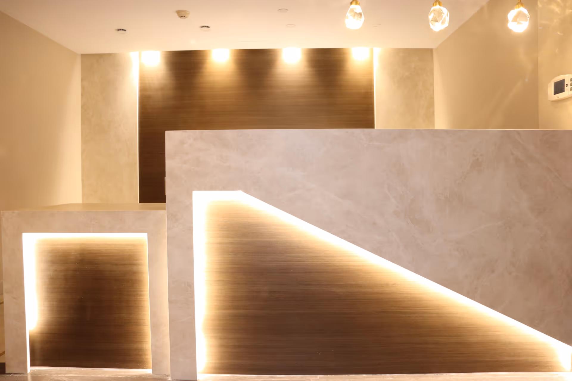 Modern reception area with illuminated wood panels and marble-like counters indoors.