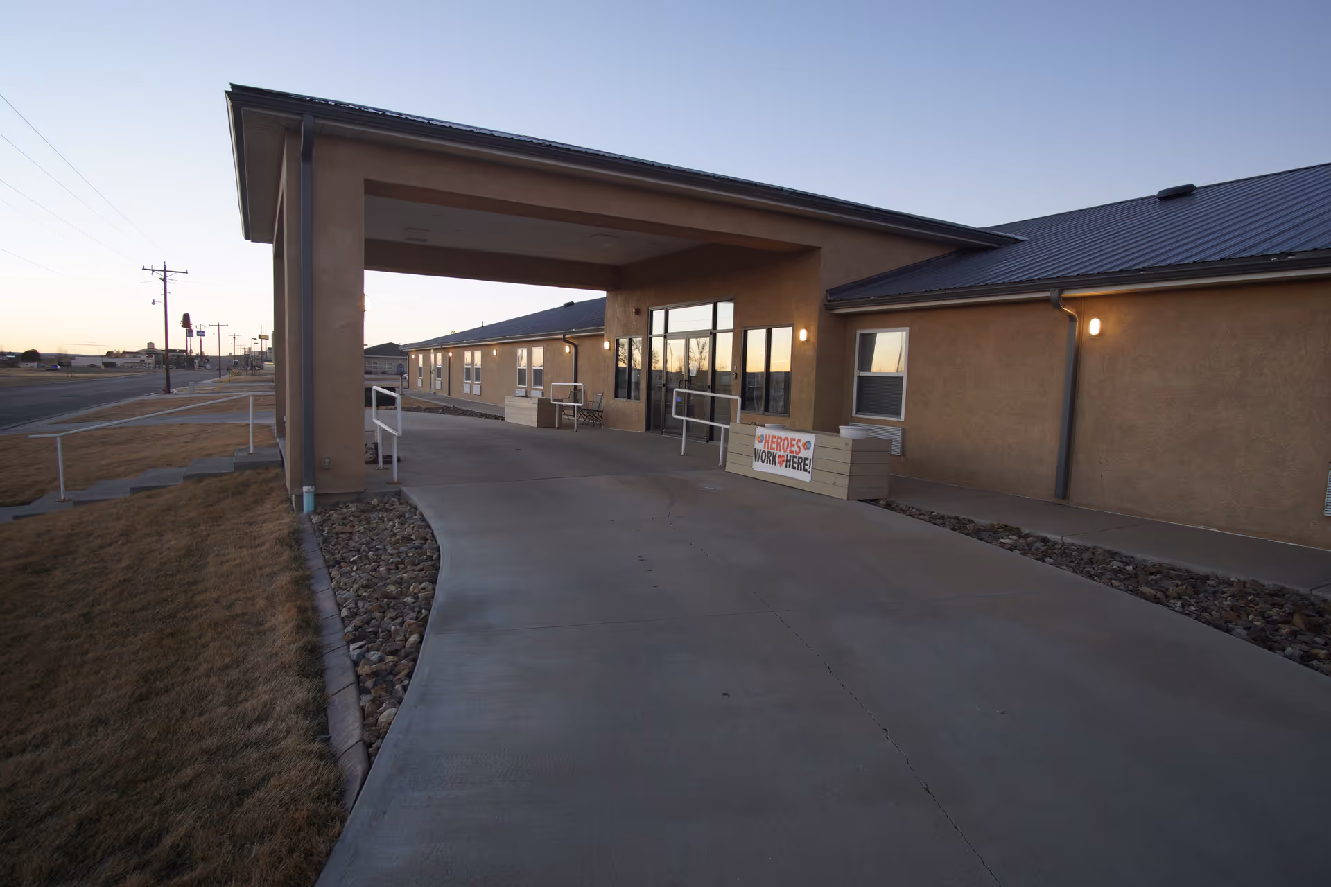 Covered entrance and driveway leading to a single-story assisted living building with a "Heroes Work Here" sign.