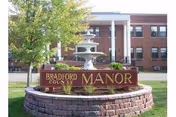 Exterior view of a brick nursing facility with a circular stone sign and fountain.