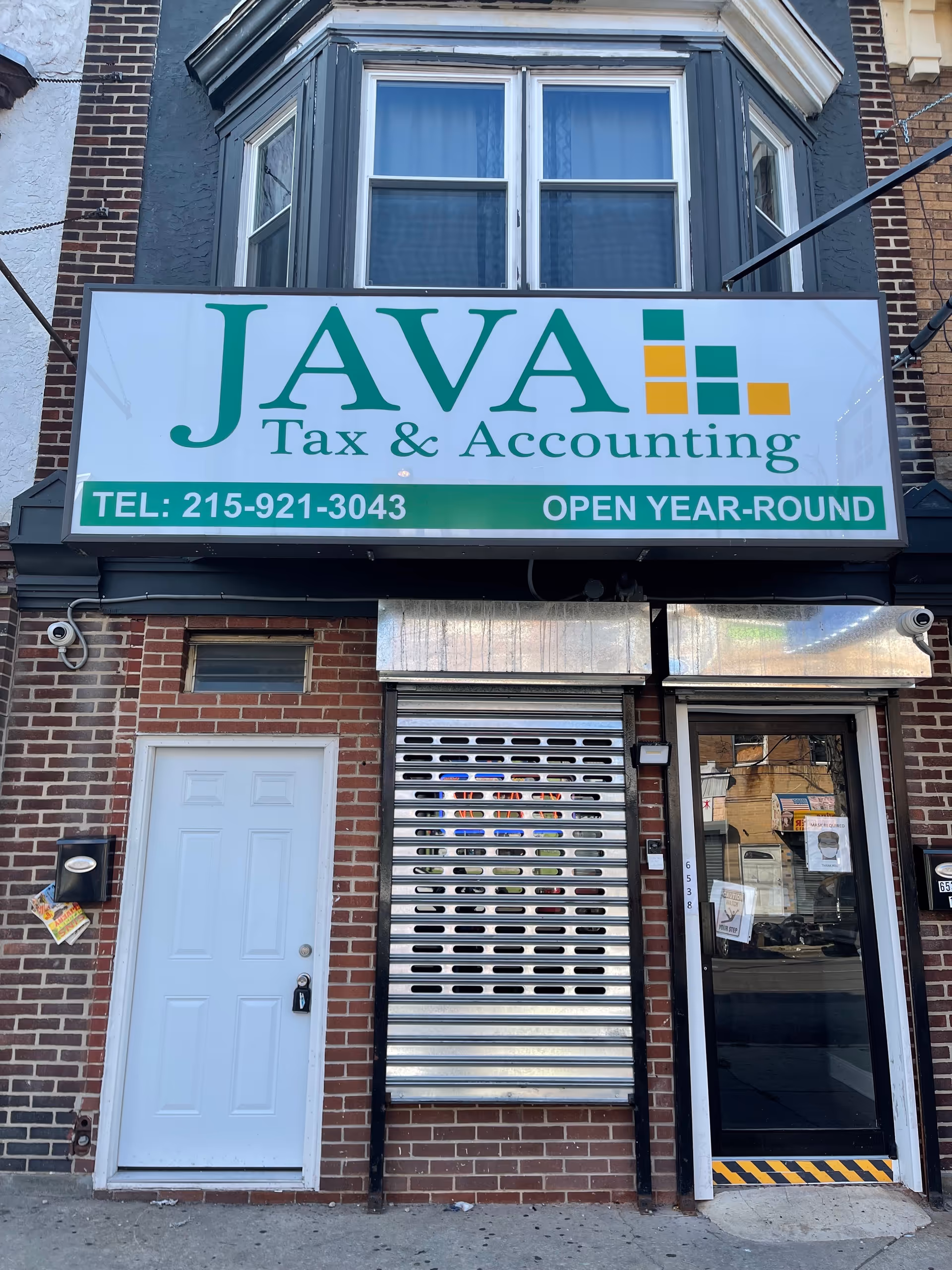 Brick building storefront with a large JAVA Tax and Accounting sign and metal roll shutter.