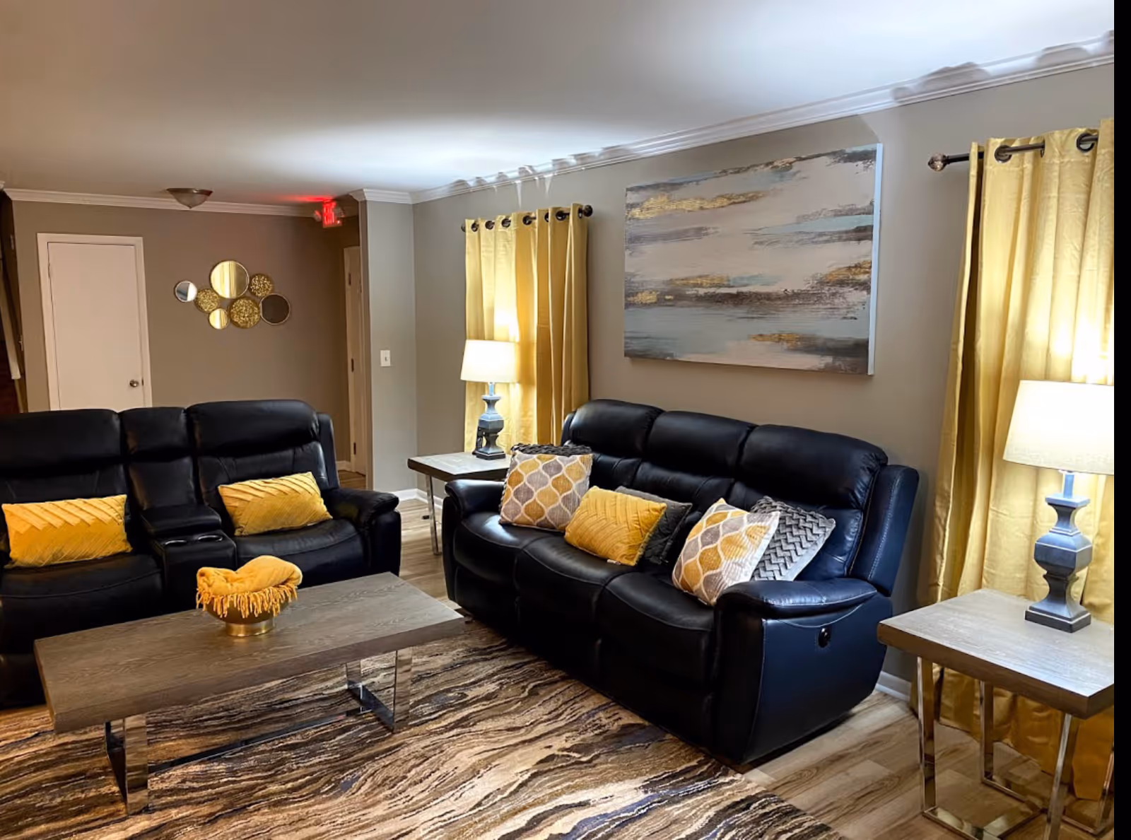 Cozy living room with black leather sofas, yellow accents, and abstract wall art.