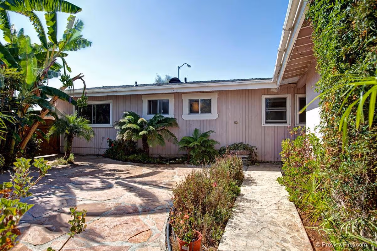 Outdoor courtyard of Right Choice Senior Living Clairemont with pink exterior, tropical plants, and stone paving.