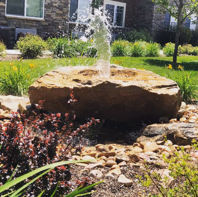 Stone fountain jet rising from a large rock in a landscaped outdoor courtyard near Covington Lehi.