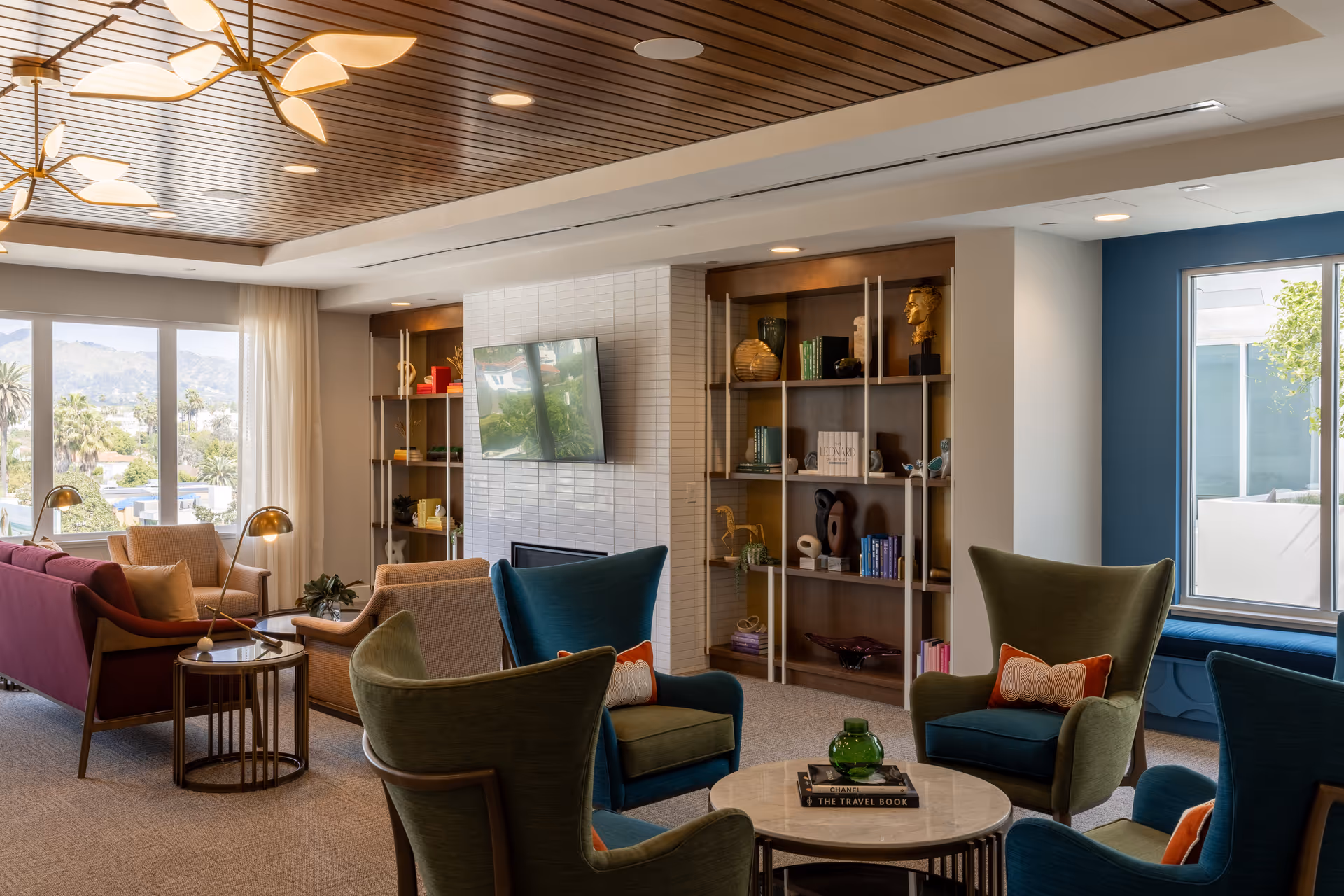 Bright senior living lounge with colorful chairs, couches, shelves, and a wall-mounted TV.