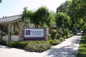 Exterior view of Westchester Gardens senior living facility with sign, sidewalk, and greenery.