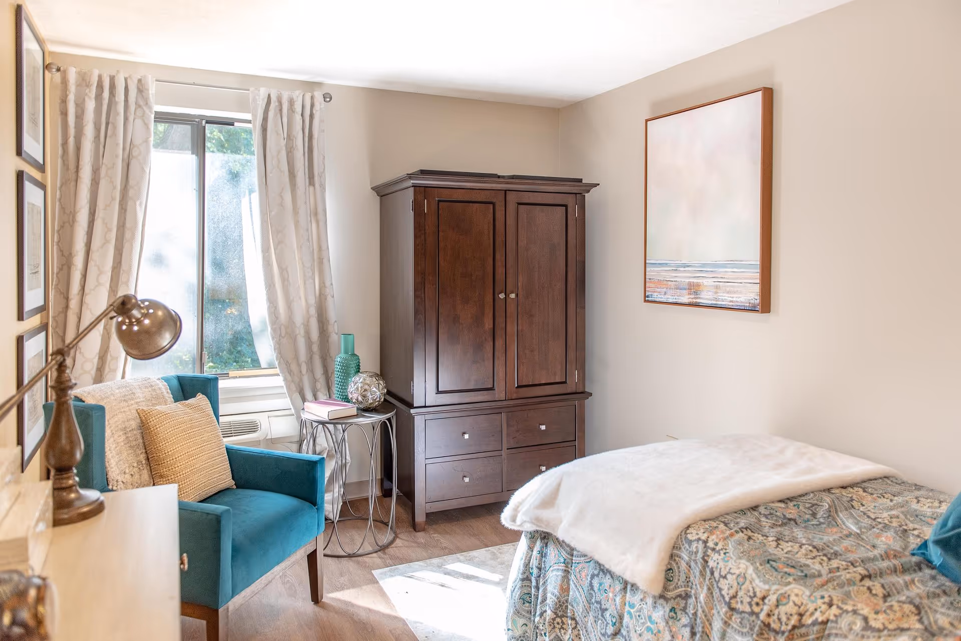 Cozy bedroom with teal chair, dark armoire, bed, and large window with curtains.