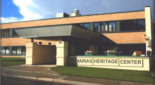 Brick senior living facility exterior with a covered entrance and heritage center sign.