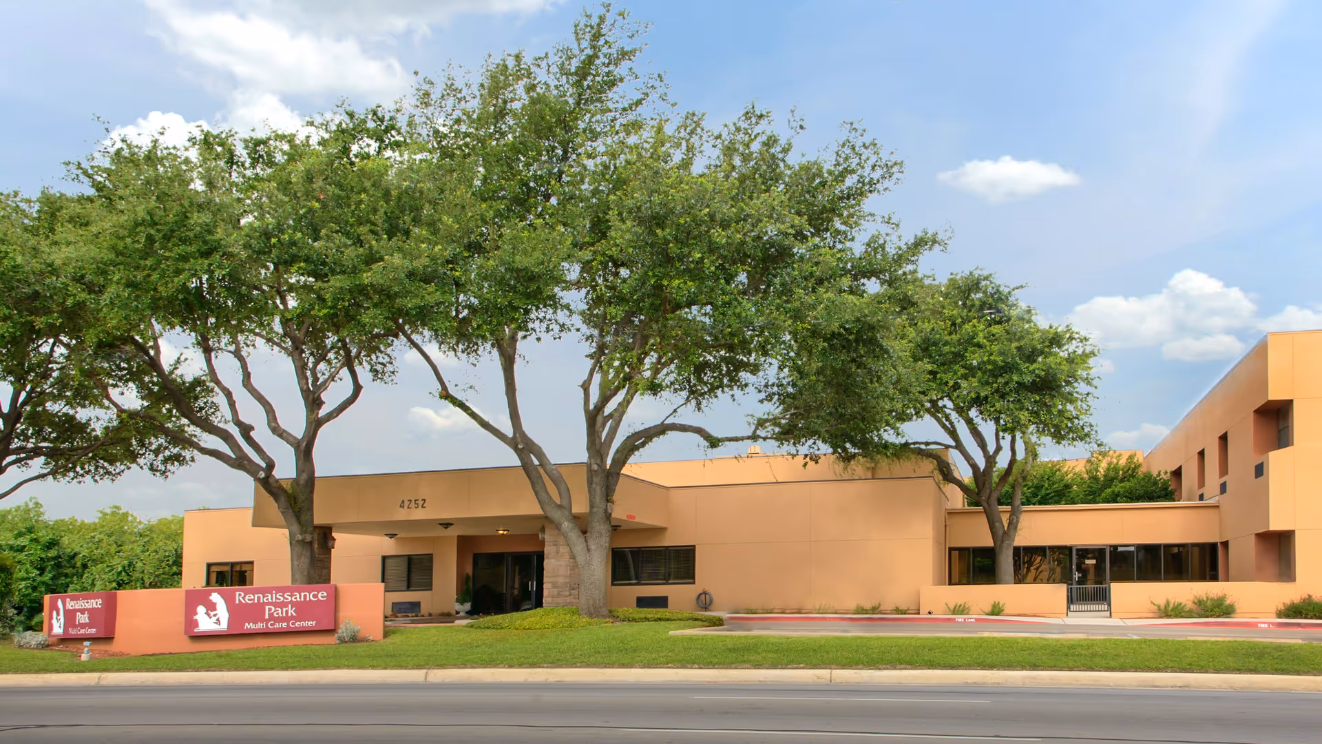 Exterior view of Renaissance Park Multi Care Center building with a beige facade, several large trees in front, and a sign displaying the facility's name near the street.