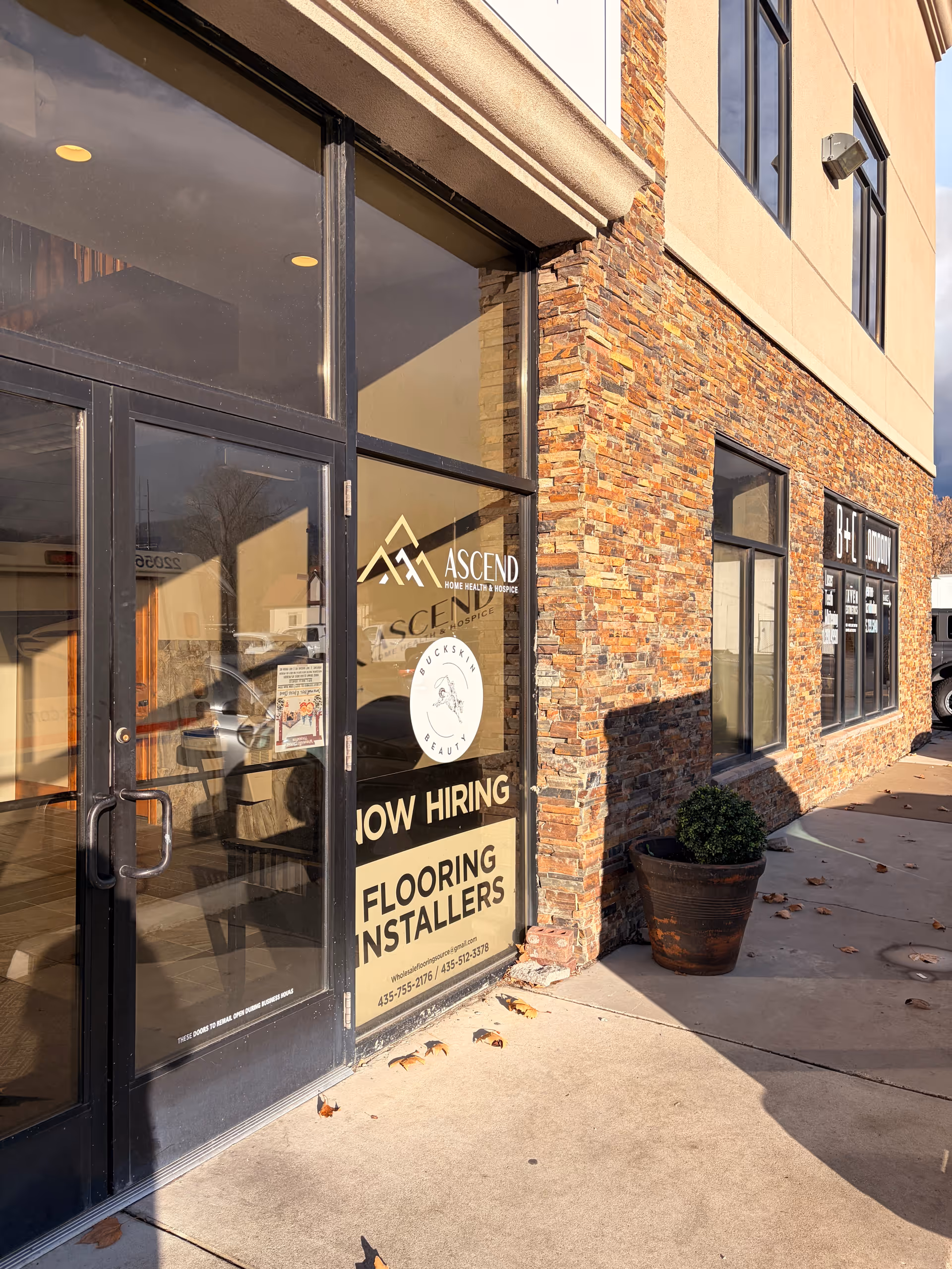 Brick storefront with glass doors displaying Ascend Home Health & Hospice and a Now Hiring sign