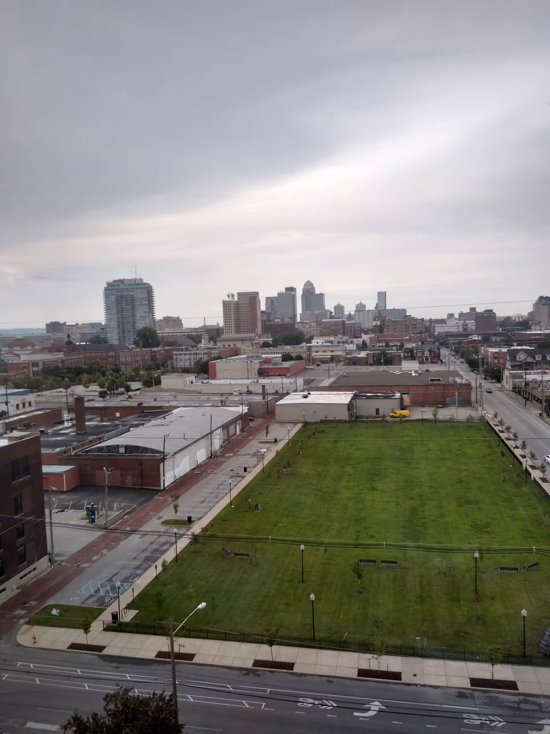 City skyline above a grassy park with benches and sidewalks.