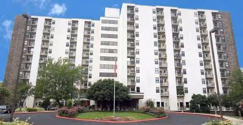 Tall white residential building with balconies, manicured landscaping, and a circular driveway at Windlands South.