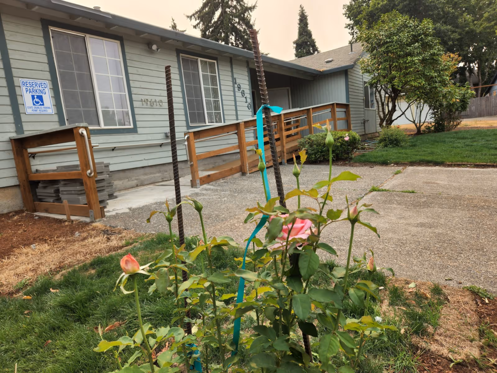 Front exterior of a light-blue facility with a ramp and blooming roses.