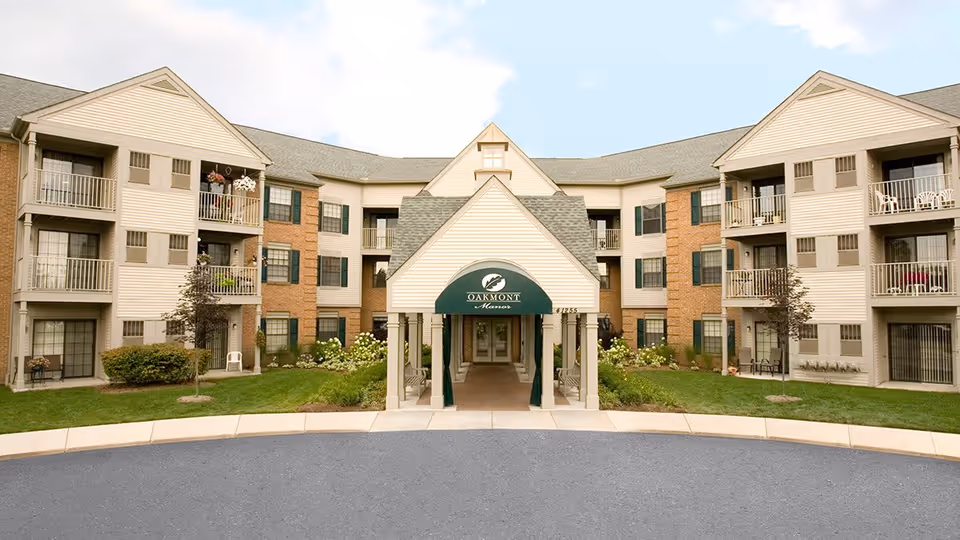 Front exterior view of Oakmont Manor Senior Community building with a covered entrance, three stories, balconies, and landscaped greenery.