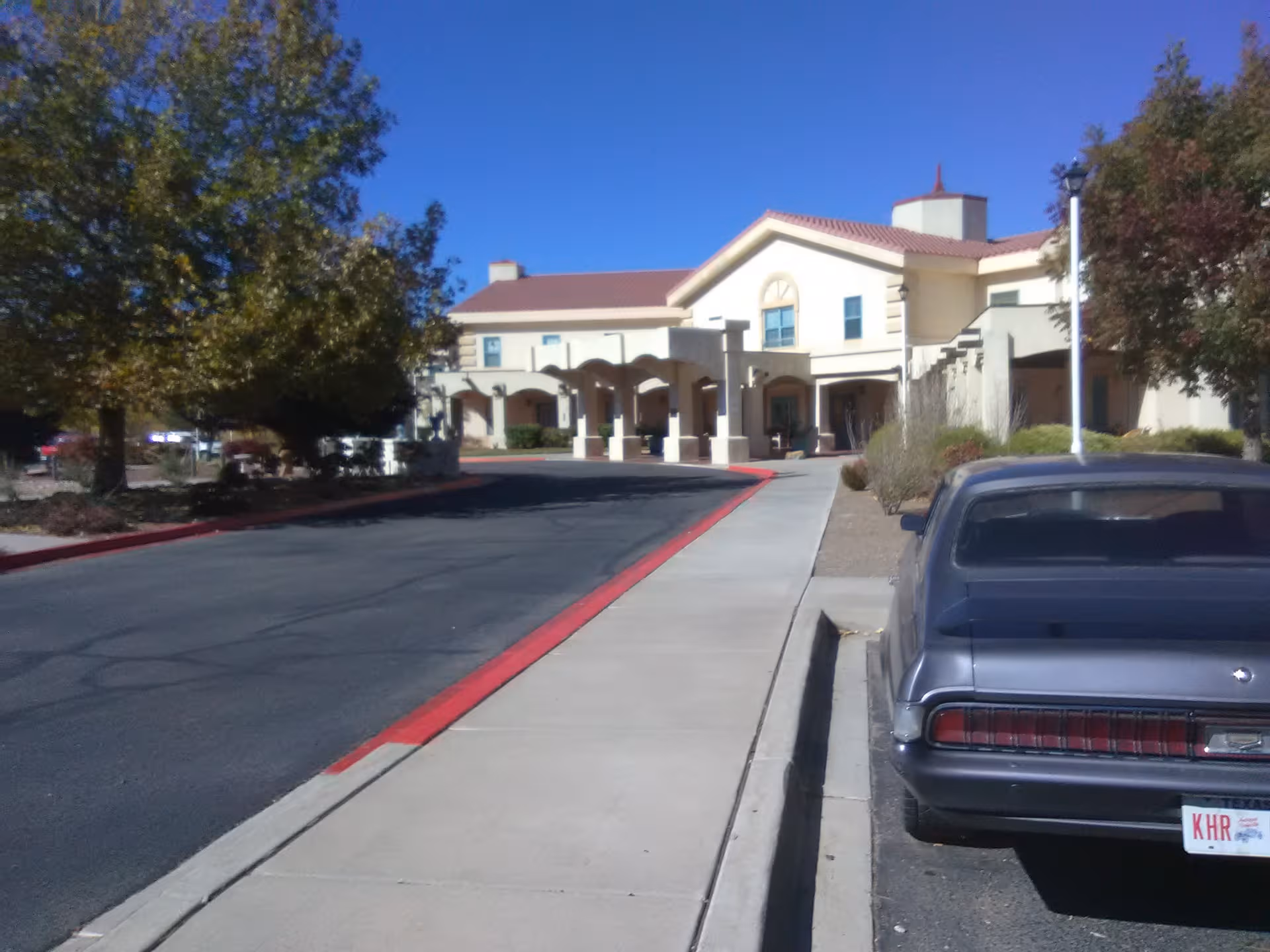Exterior of The Village at Alameda senior living facility with driveway and parked car.
