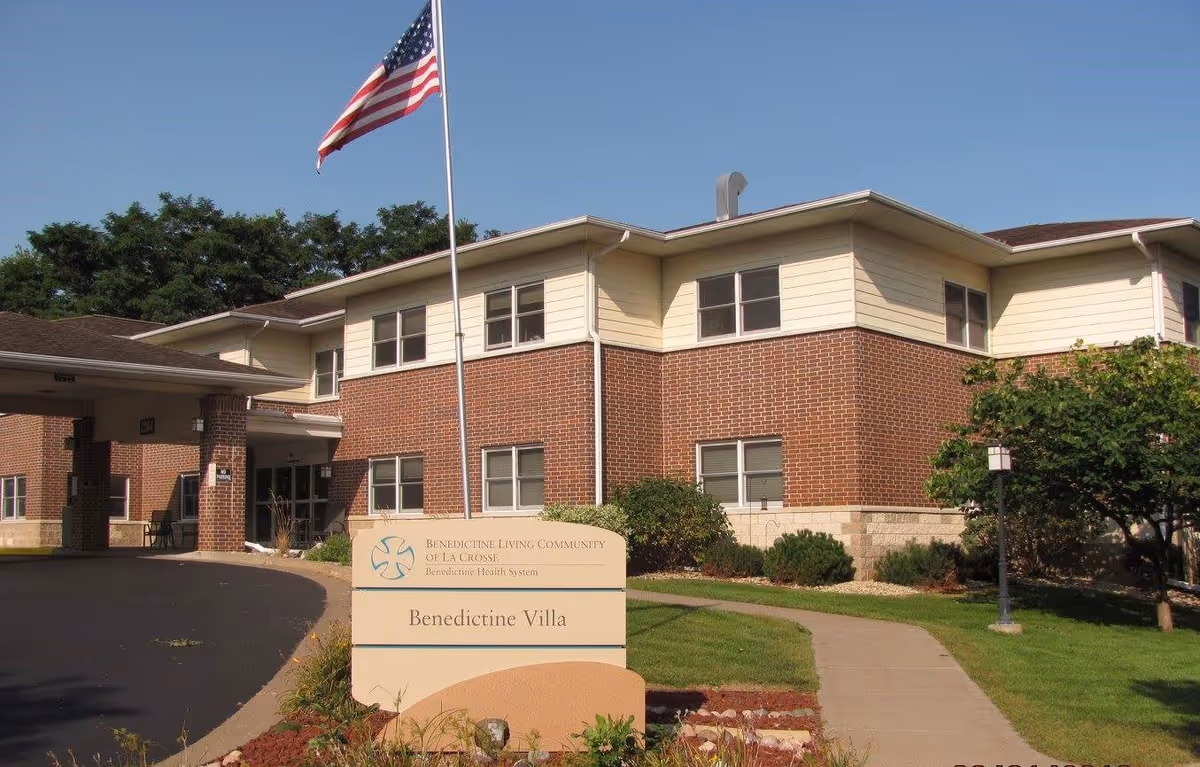 Front exterior of a two-story brick senior living building with an American flag and a sign reading Benedictine Villa at the entrance.