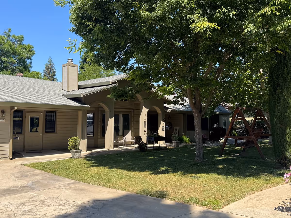 Exterior of a senior living facility with a shaded porch and yard seating.