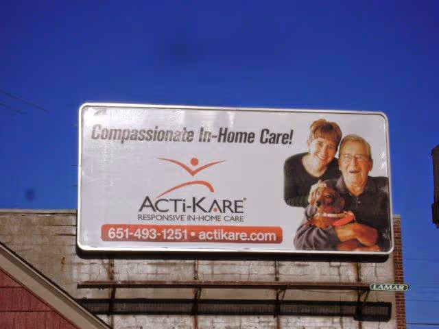 Outdoor billboard on a building promoting Acti-Kare In-Home Care with elderly couple.