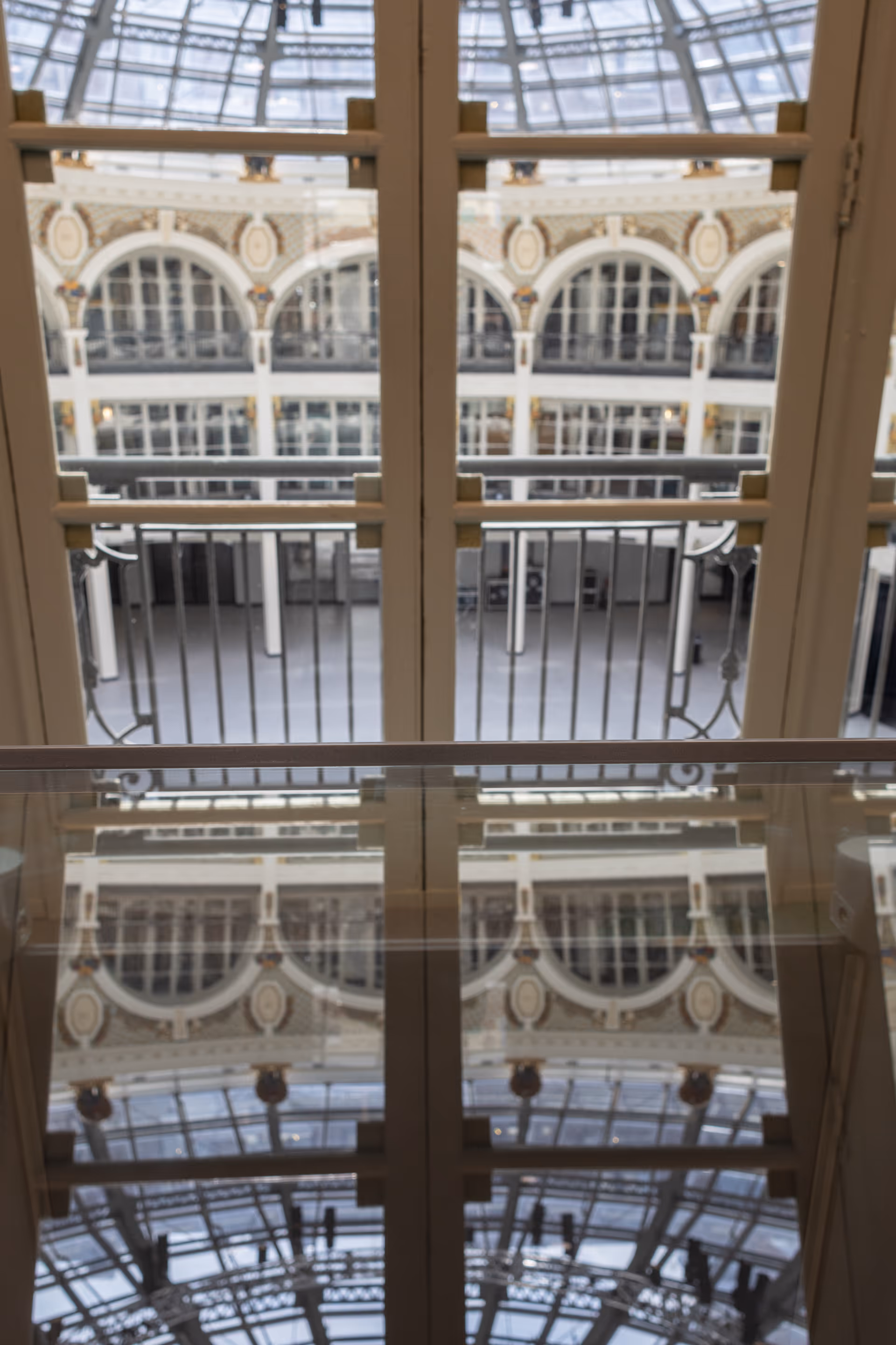 Interior atrium with ornate arches and a glass roof, viewed through doors.