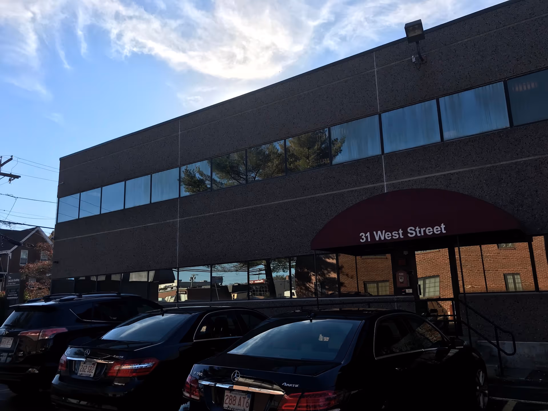 Two story building facade with large windows, maroon awning reading 31 West Street, and parked cars.