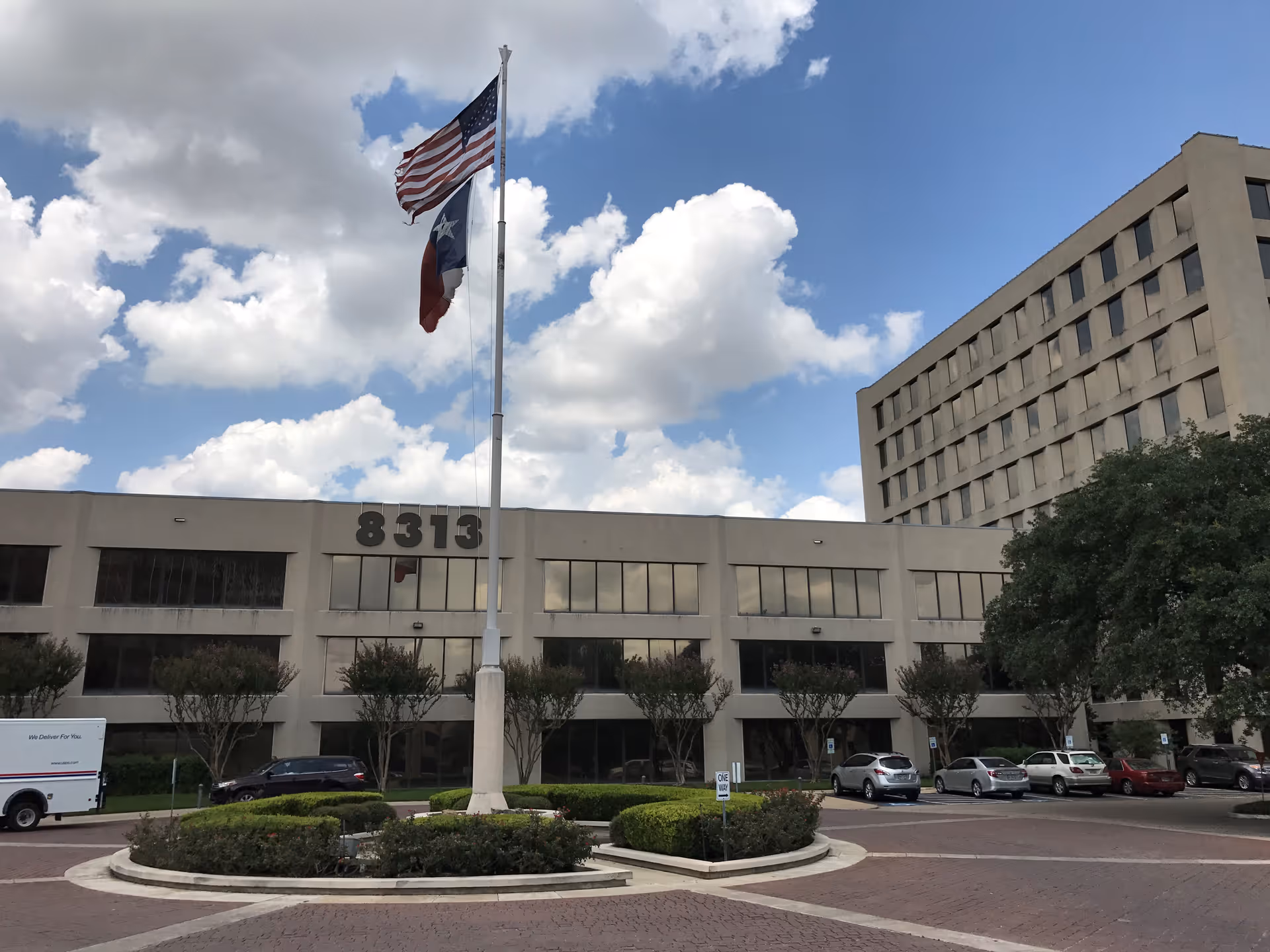 Exterior view of a large beige office building with a flagpole in front.