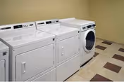 Row of white front-loading laundry machines in a small, clean laundry room.