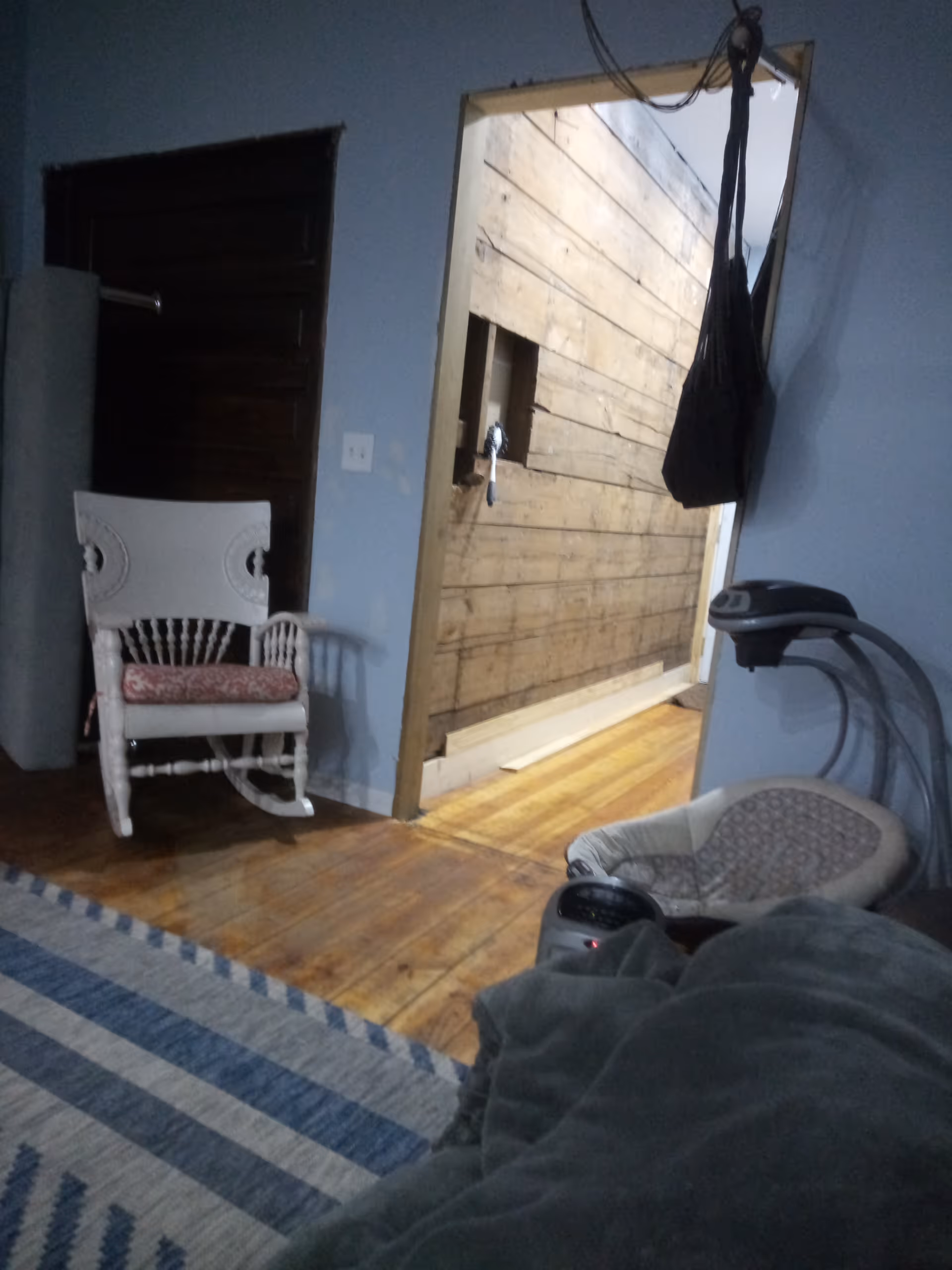 Blue walls in a living area with striped rug, rocking chair, treadmill, and an open doorway.