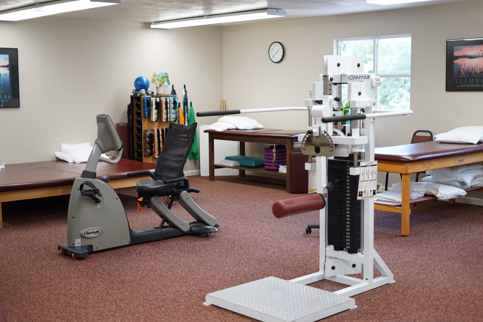 Indoor physical therapy room featuring exercise equipment, treatment tables, and storage shelving.