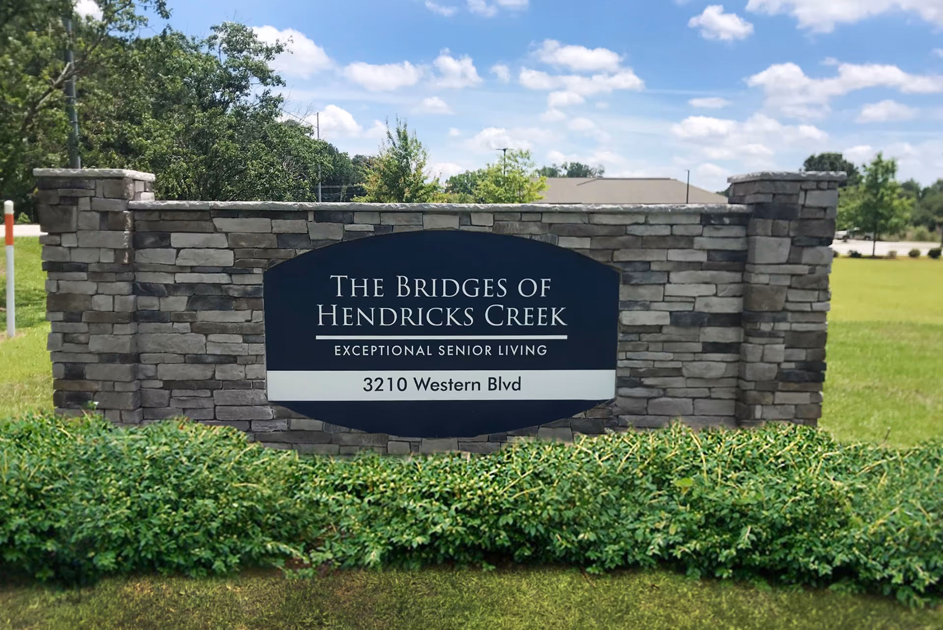 Stone entrance sign reads The Bridges of Hendricks Creek, Exceptional Senior Living, 3210 Western Blvd.