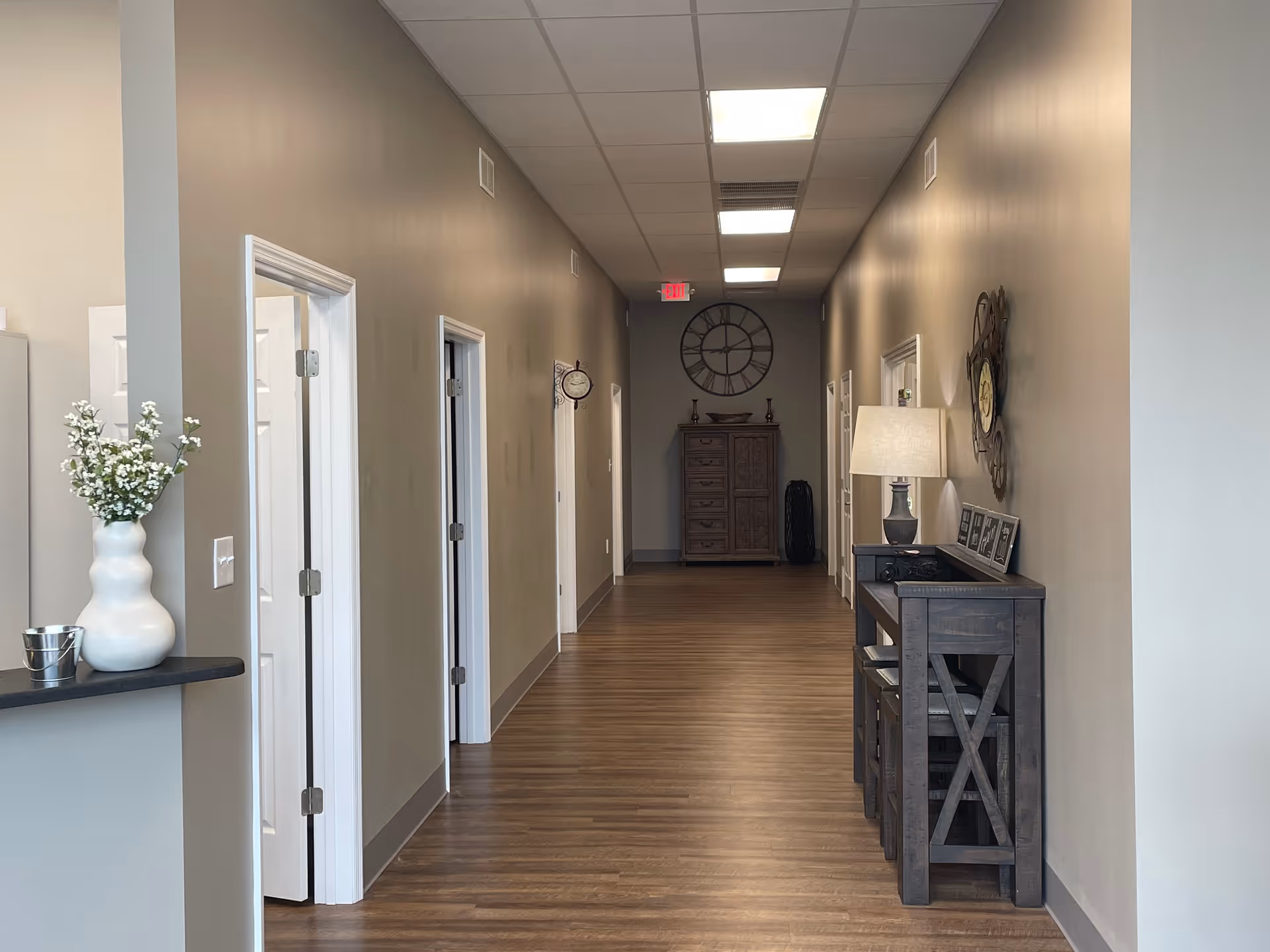 Long hallway in a senior living facility with doors, decor, and a console table.