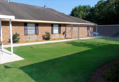 Brick building exterior with windows, a chain-link fence, and manicured lawn.