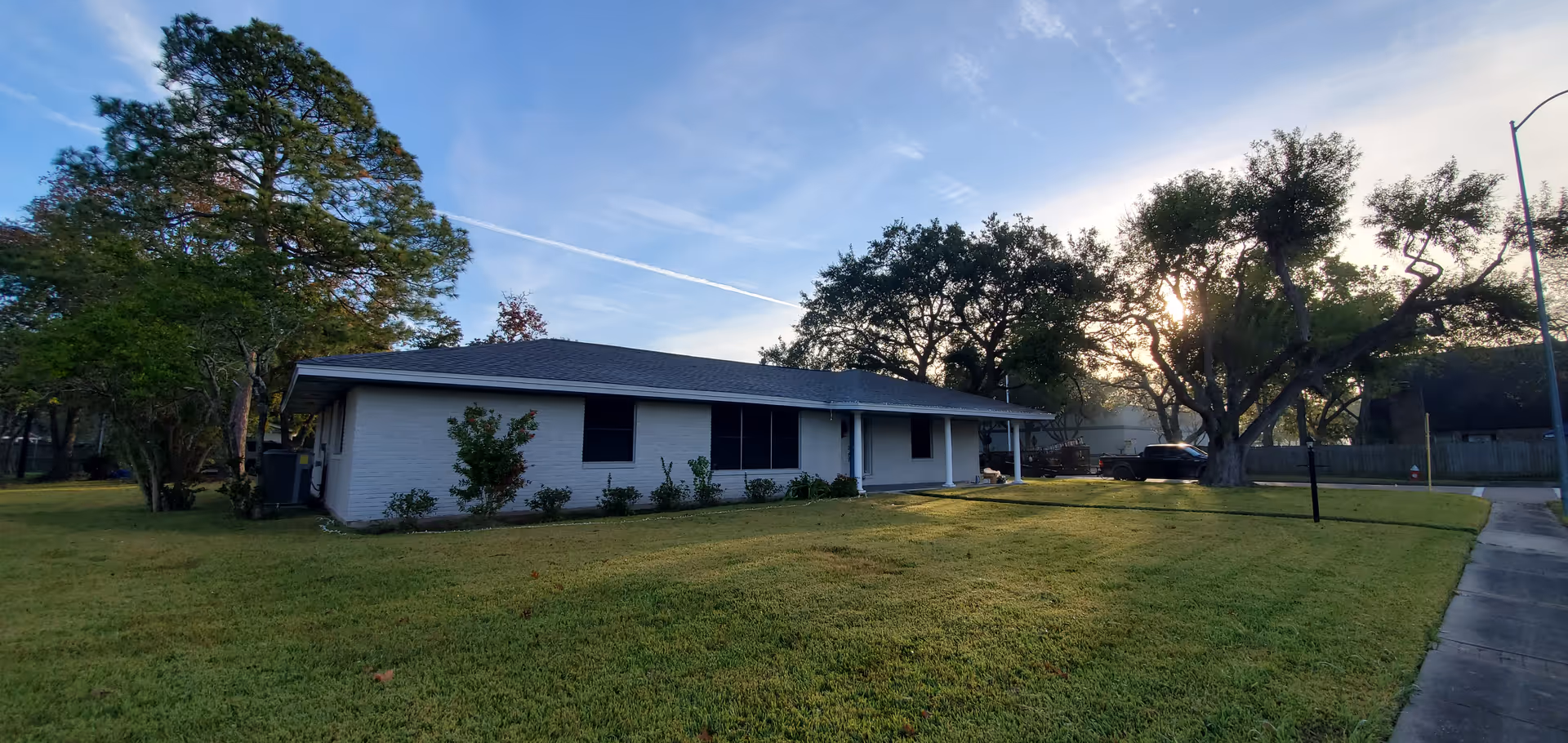 Single-story white building with a large grassy yard and trees in front.