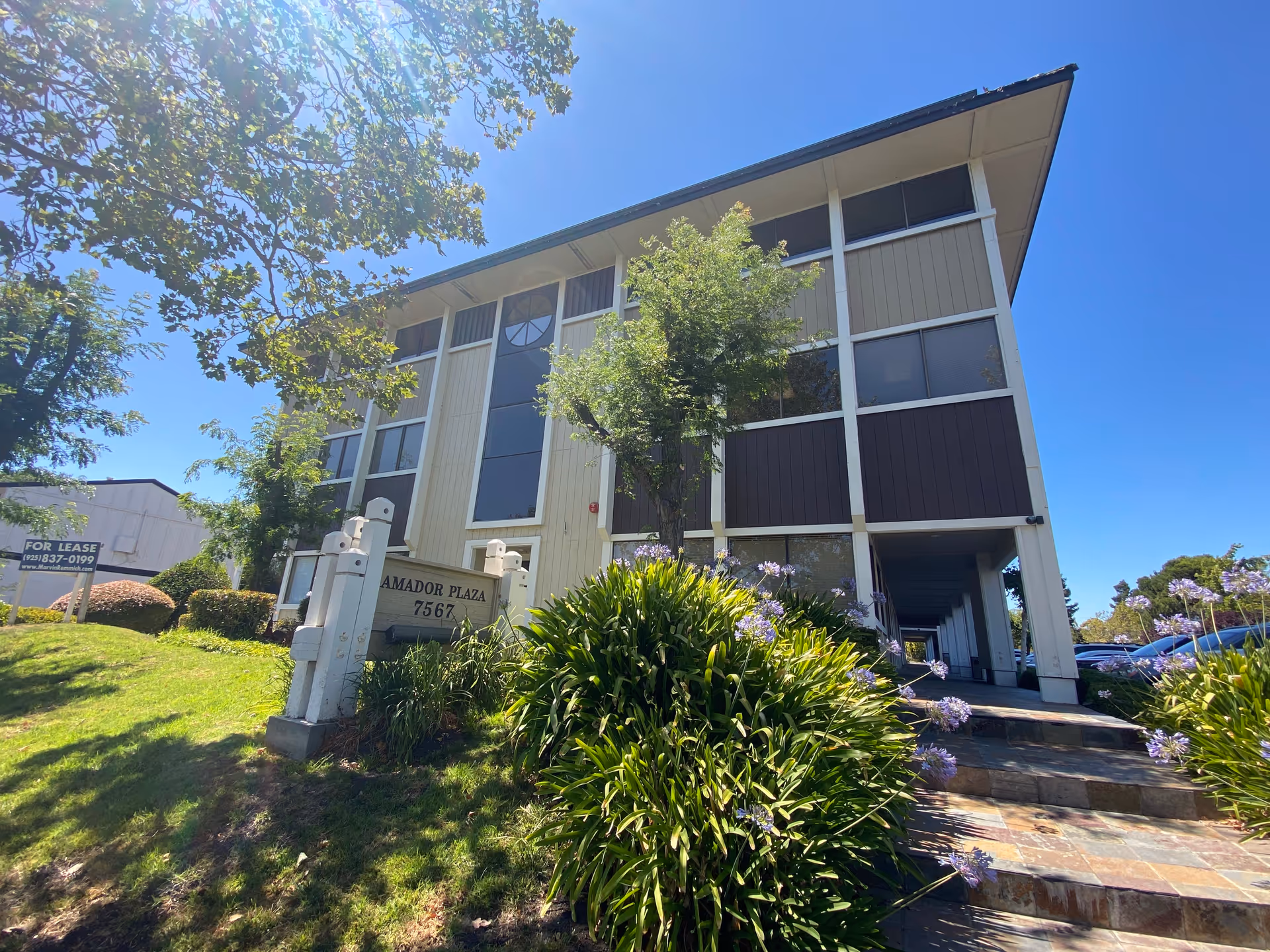 Three-story senior living building with glass windows, landscaped entry, and clear blue sky.