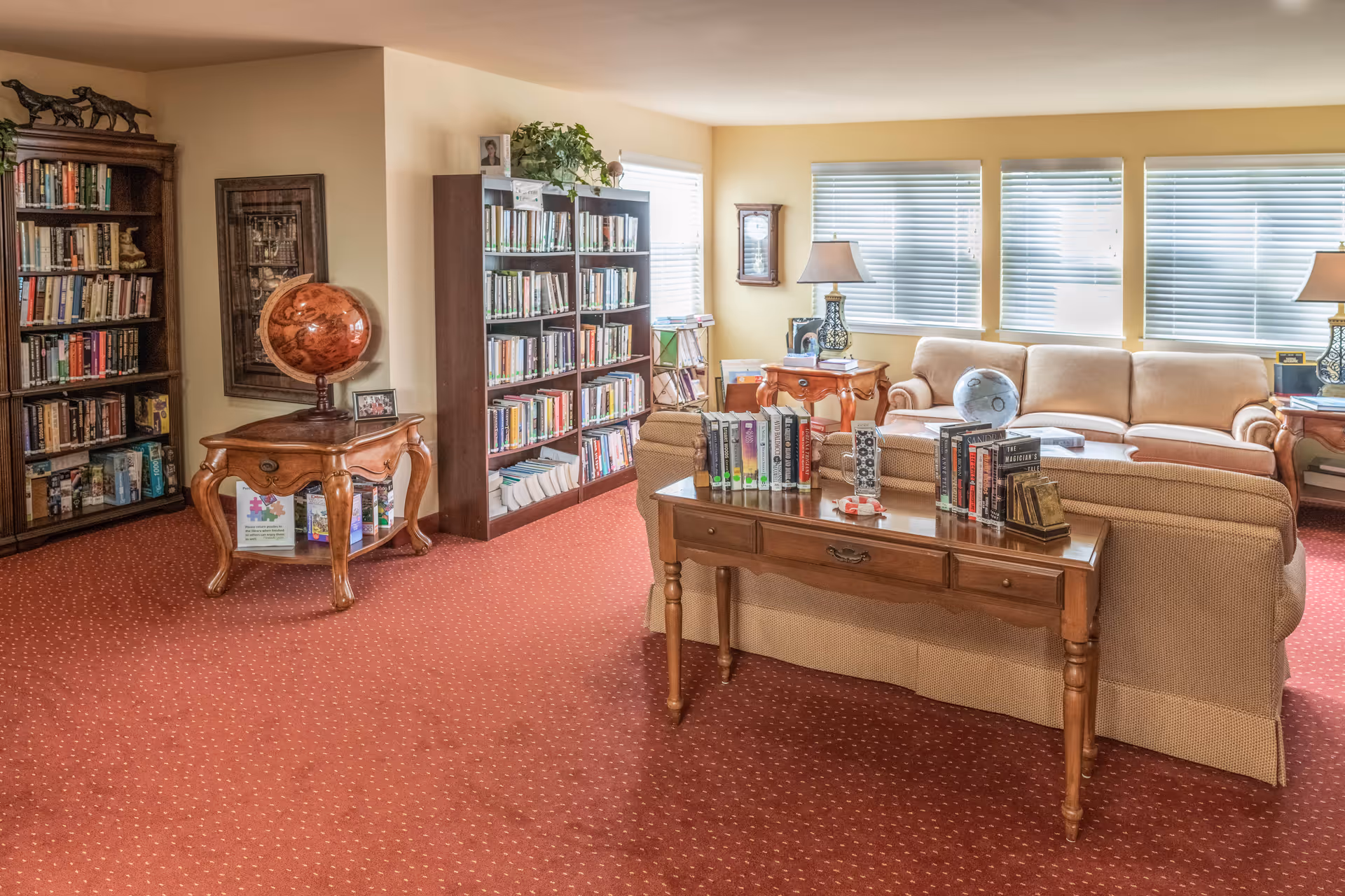 Bright communal living room/library with bookshelves, sofas, side tables, lamps and a globe.