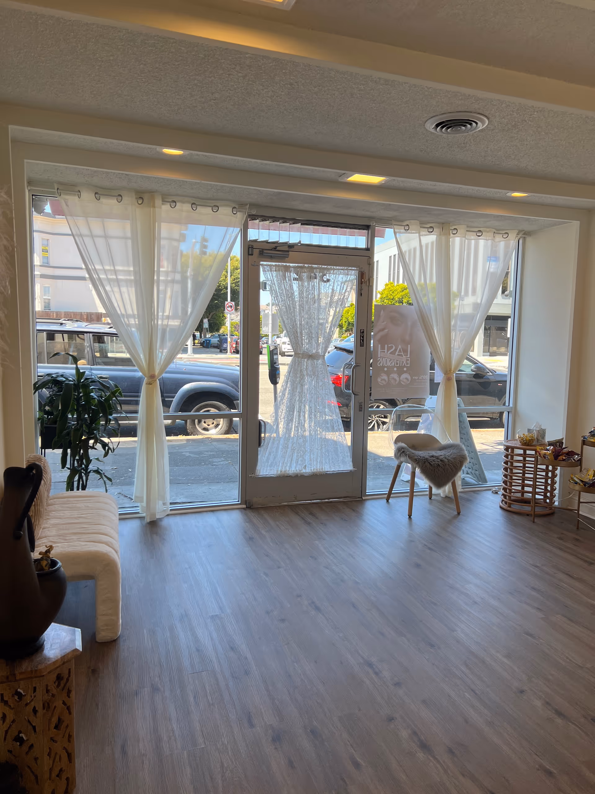 Bright interior lobby with glass doors, sheer curtains, seating, and a street view.