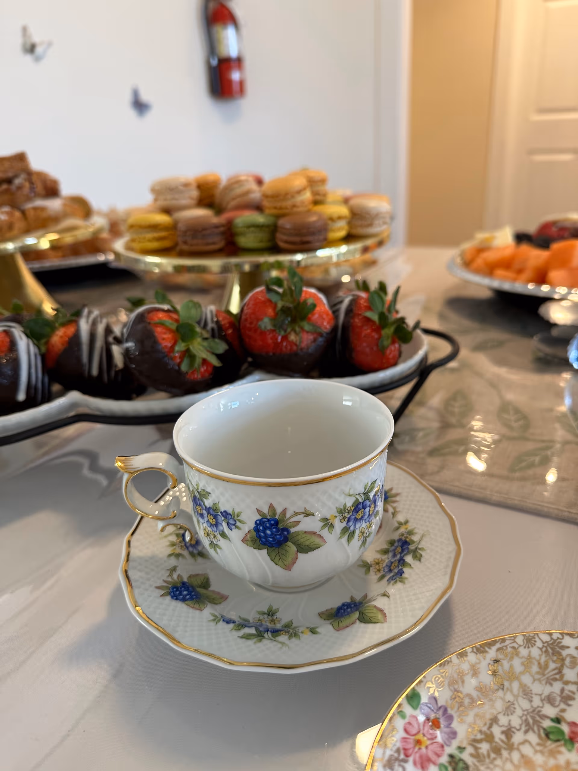 Elegant table spread with teacup, pastries, and strawberries in a dining setting.