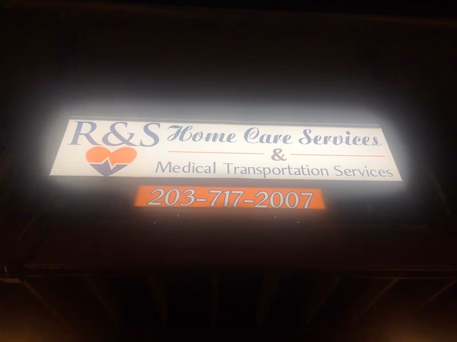 Night-lit sign on building front reads R&S Home Care Services and Medical Transportation.