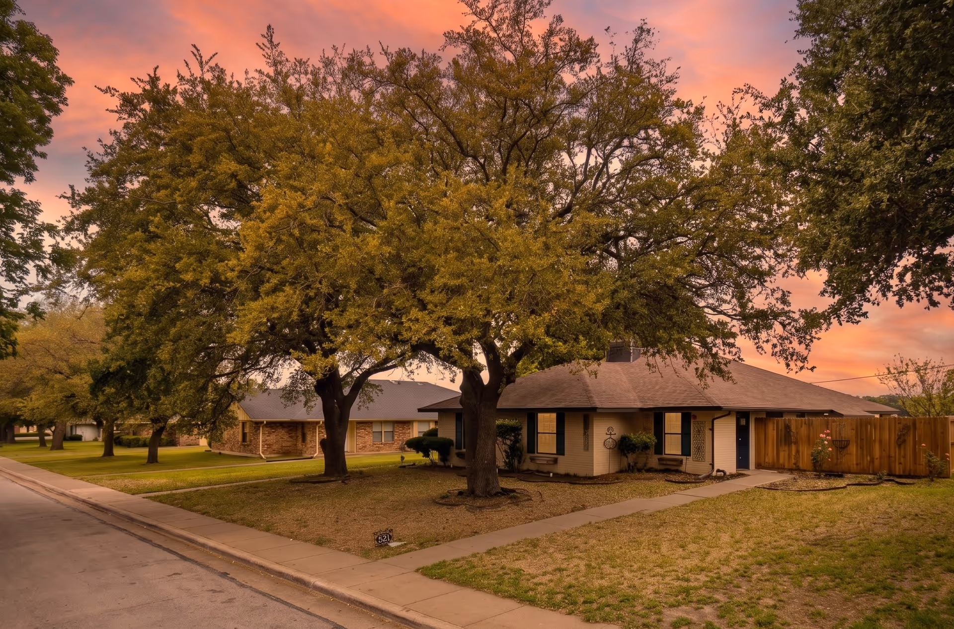 A single-story residential facility with brick exterior, trees, and a front yard at sunset.
