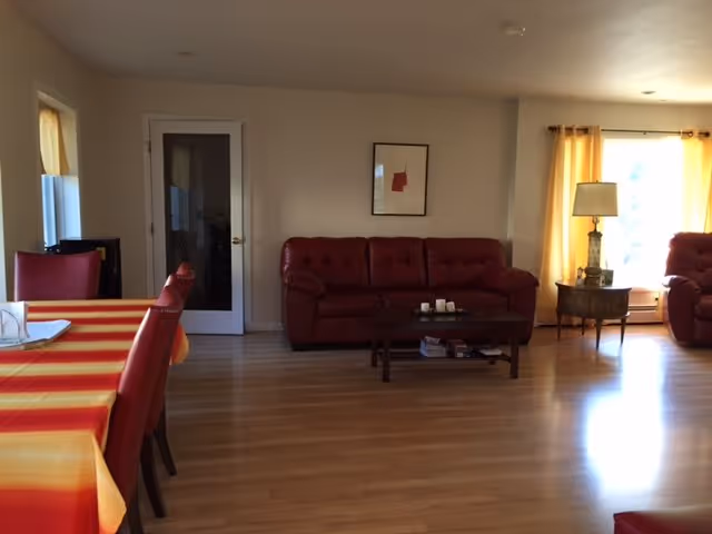Spacious living area with red couches, coffee table, lamp, and bright windows.