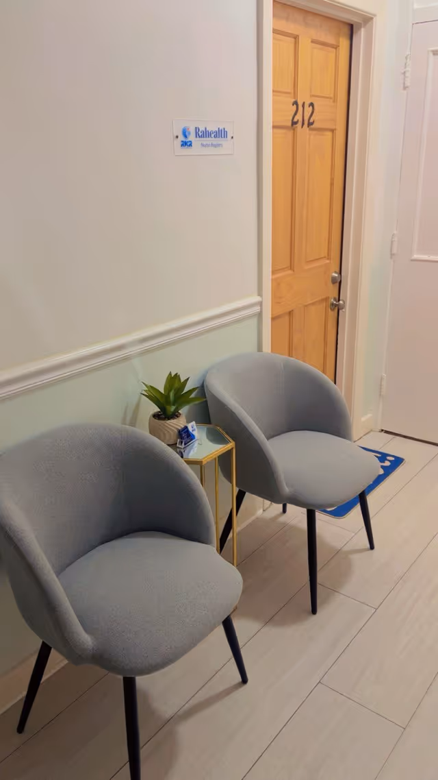 A hallway waiting area with two gray chairs and a small side table.